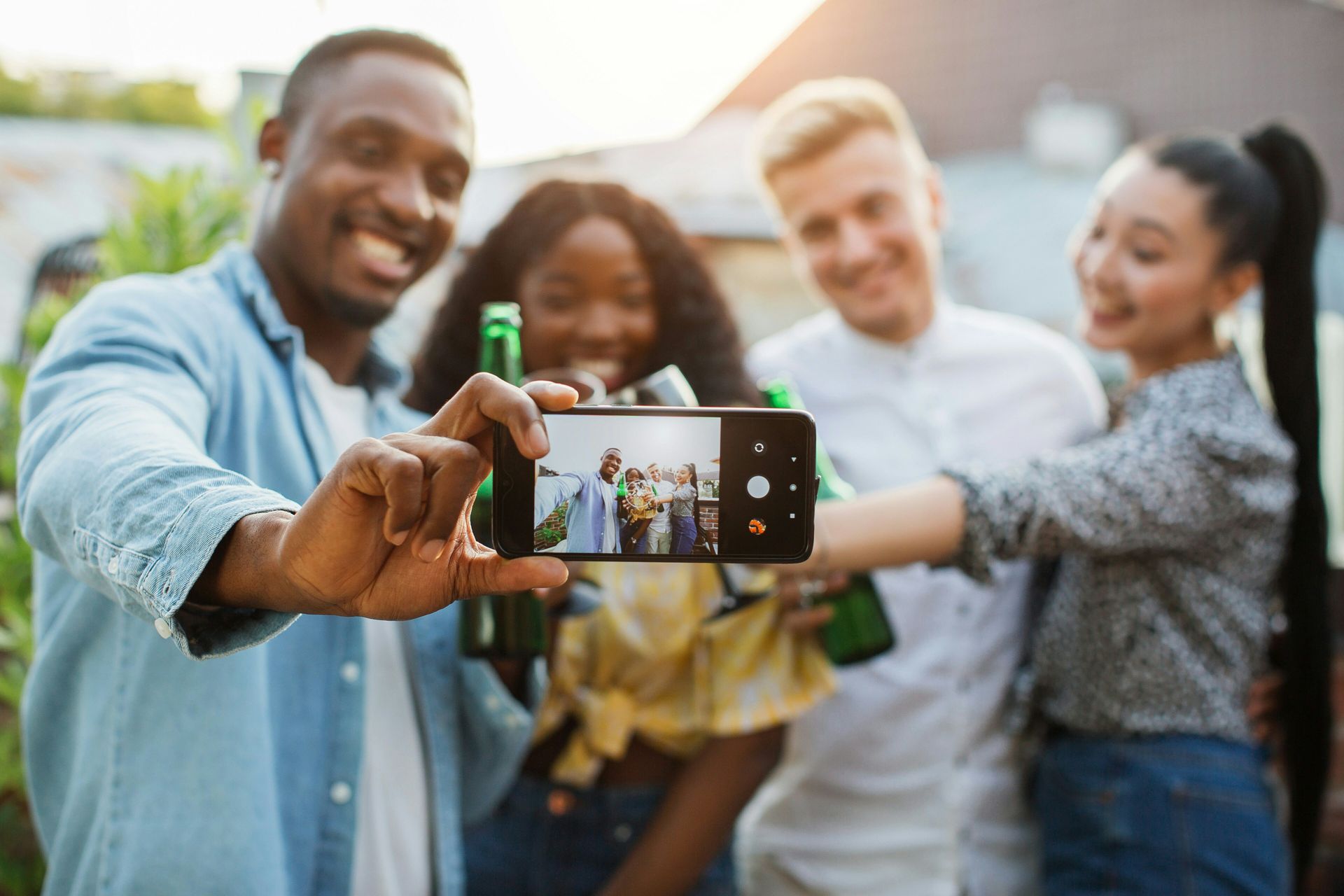 Diverse group of smiling friends taking a selfie outdoors, demonstrating social connection and positive emotional expression that contributes to mental wellbeing.