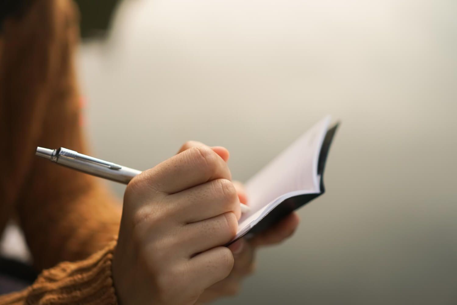 Close-up of hands holding pen and writing in notebook during therapy consultation, symbolizing the importance of asking the right questions