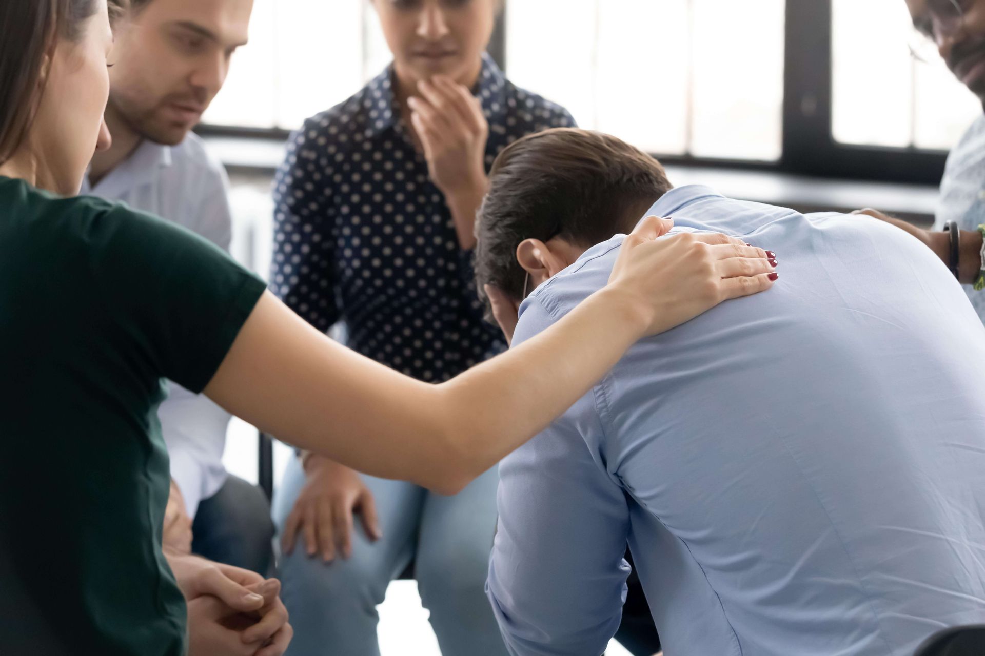 Diverse group of people in a therapy support circle with one person receiving comfort from others, showing community support for trauma healing