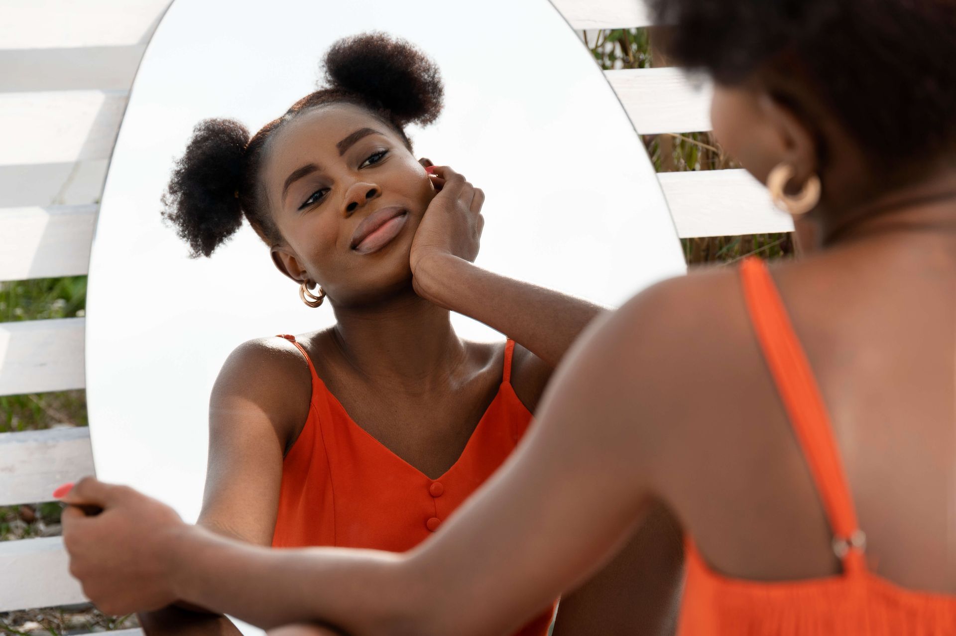 Young Black woman in vibrant orange dress sitting thoughtfully by a mirror, representing self-reflection and the journey of rebuilding self-trust after trauma