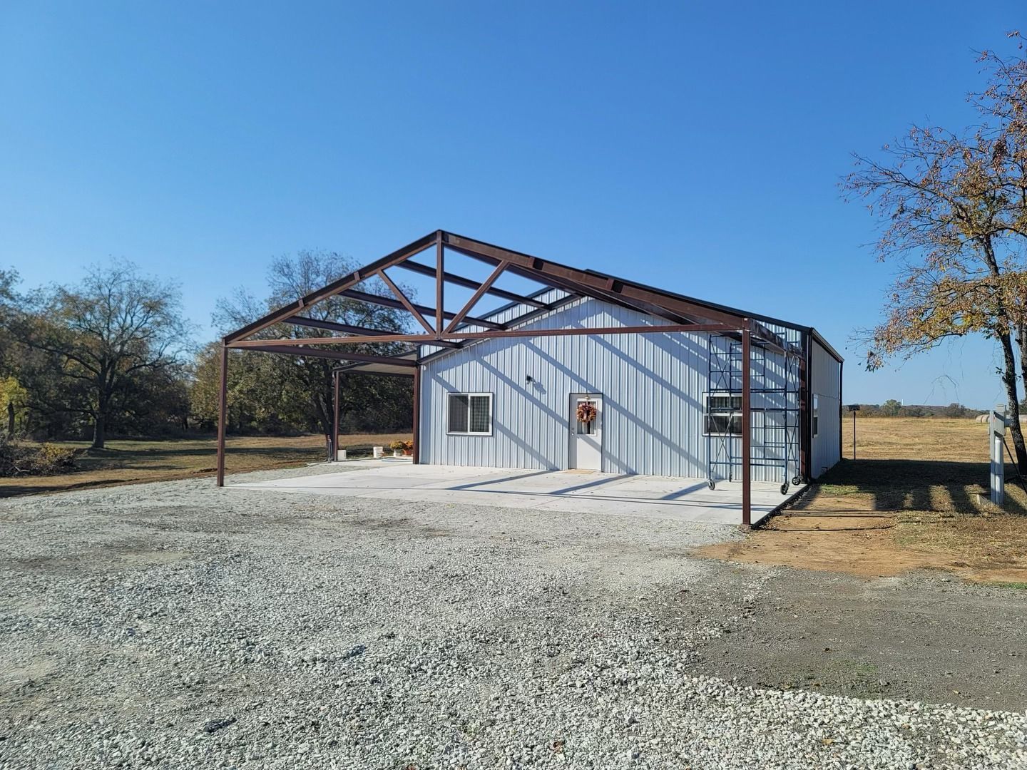 A white building with a metal frame is sitting in the middle of a gravel road.