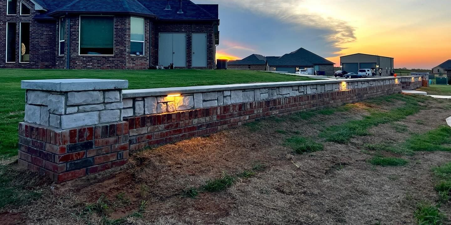 A brick wall with lights on it in front of a house at sunset.