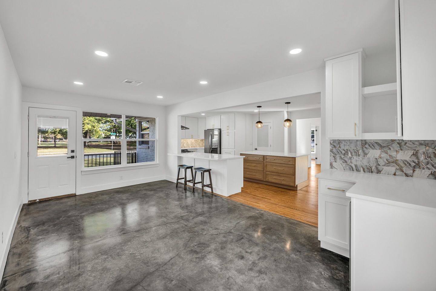 A living room with a concrete floor and a kitchen in the background.