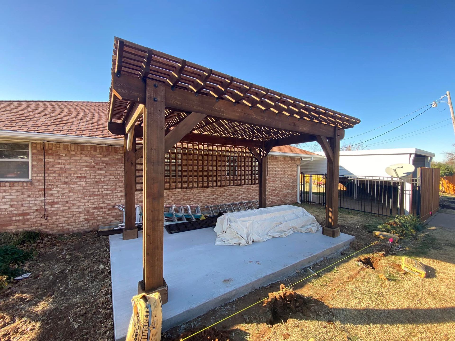 A wooden pergola is sitting in front of a brick house.