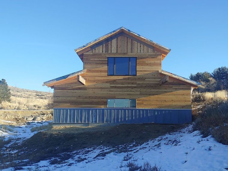 Wooden cabin under construction in a snowy landscape beneath a clear blue sky