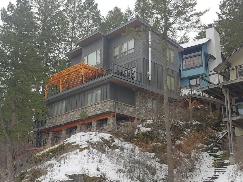 Modern house on a snowy hillside with tall pine trees nearby