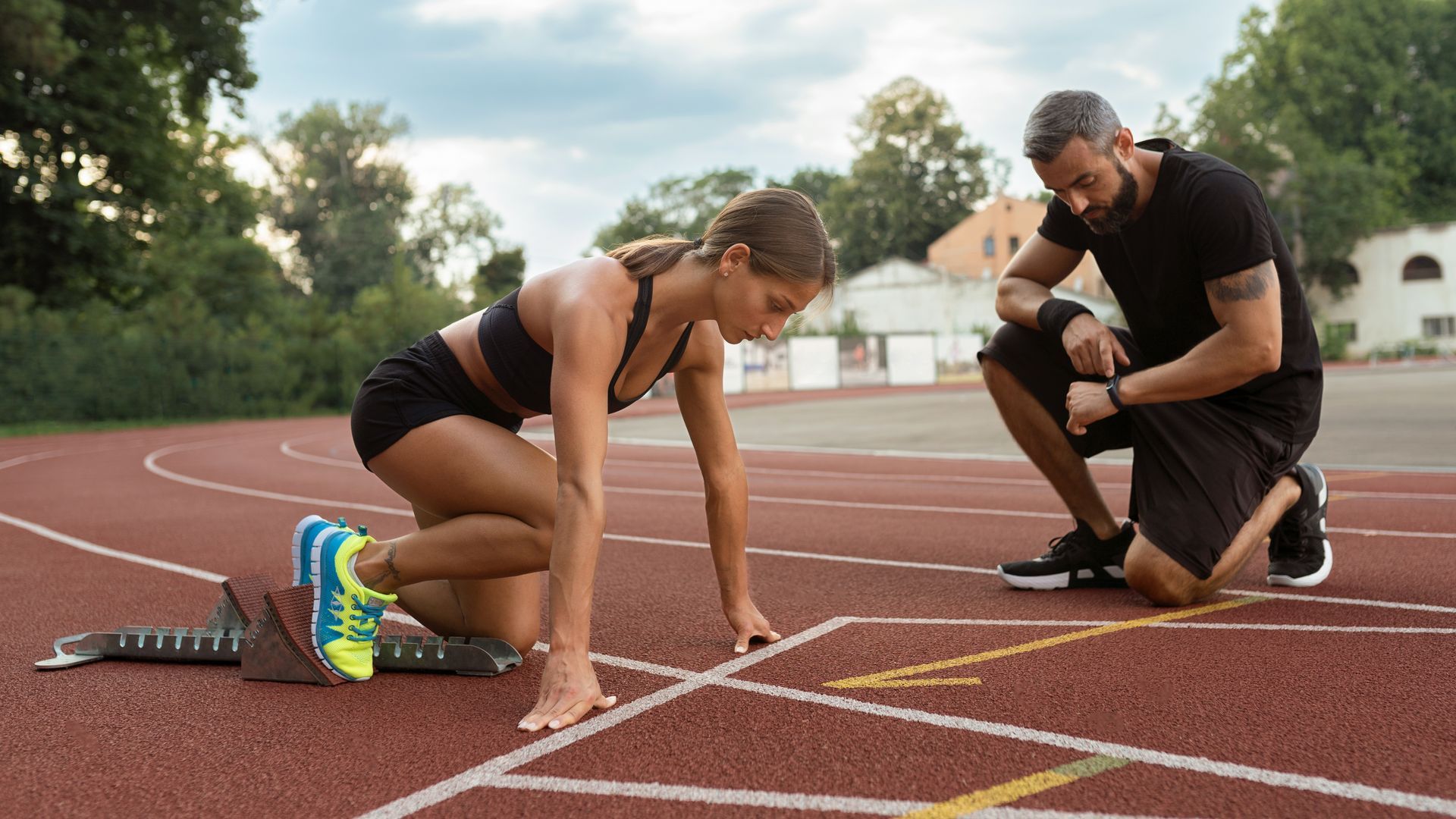 A man is helping a woman get ready to run on a track.