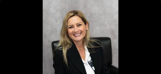A woman is sitting at a desk with a laptop and a vase of flowers.
