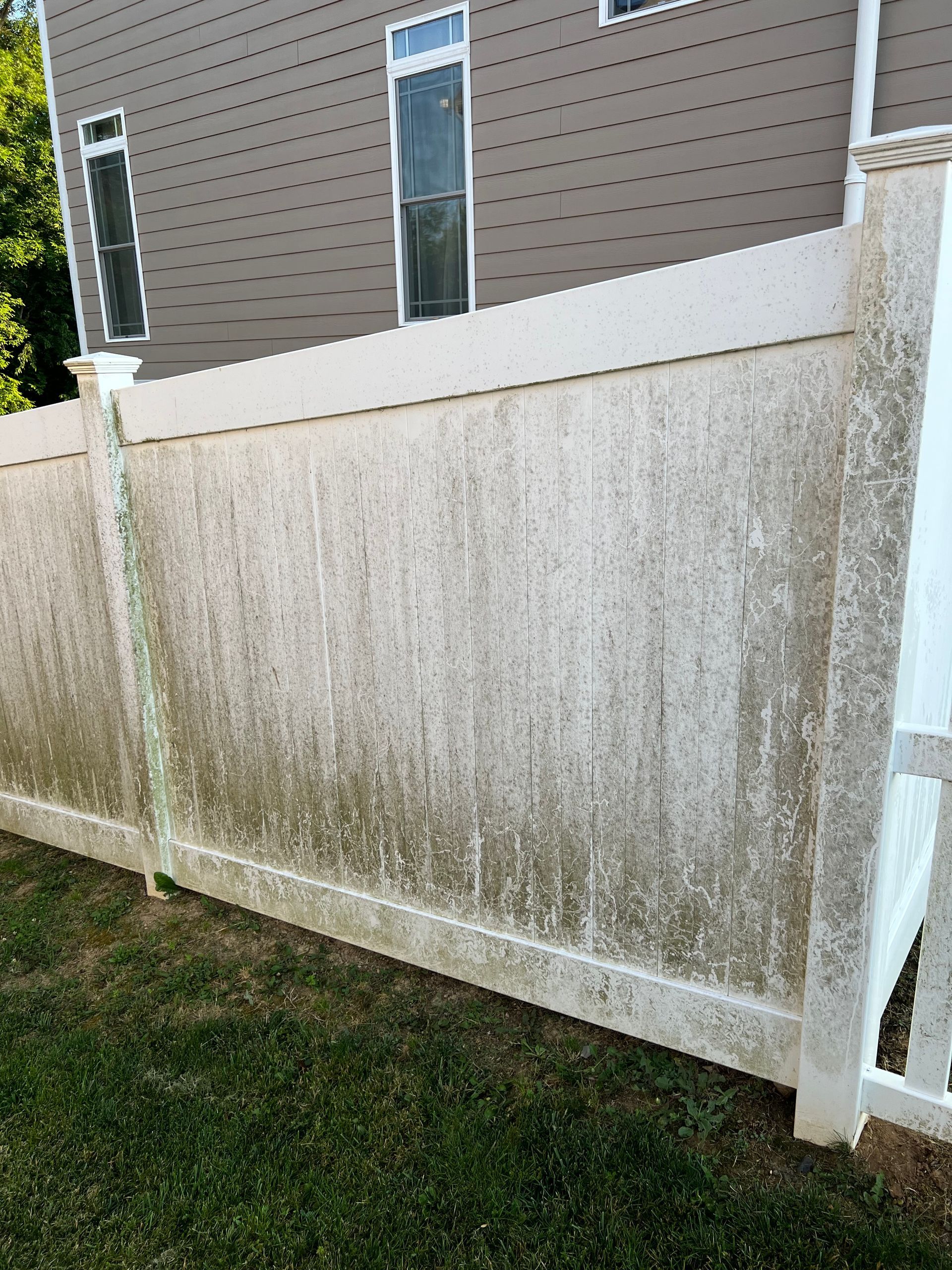 a dirty white fence is sitting in the grass in front of a house .