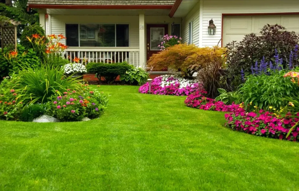 Colorful flower beds and pristine lawn in front of a white house.