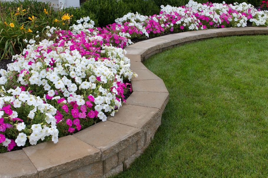 Curved stone flower bed with pink and white blooms beside a green lawn