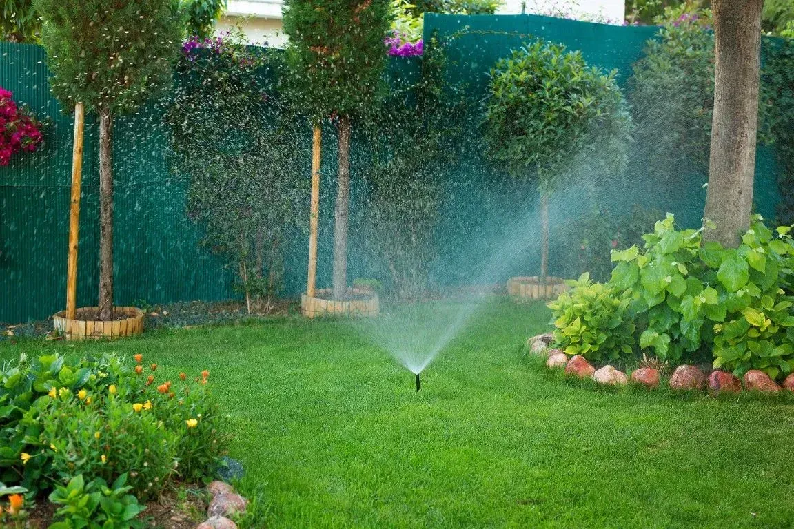 Automatic lawn sprinkler watering a lush backyard garden.