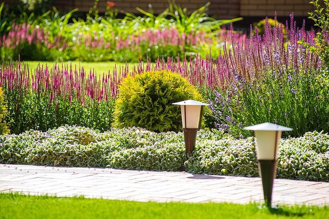 Colorful flower garden with pink and purple blooms along a paved path and two landscape lights