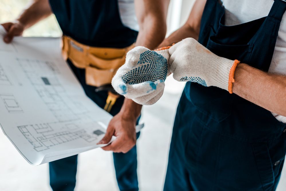 Two construction workers wearing gloves are looking at a blueprint.
