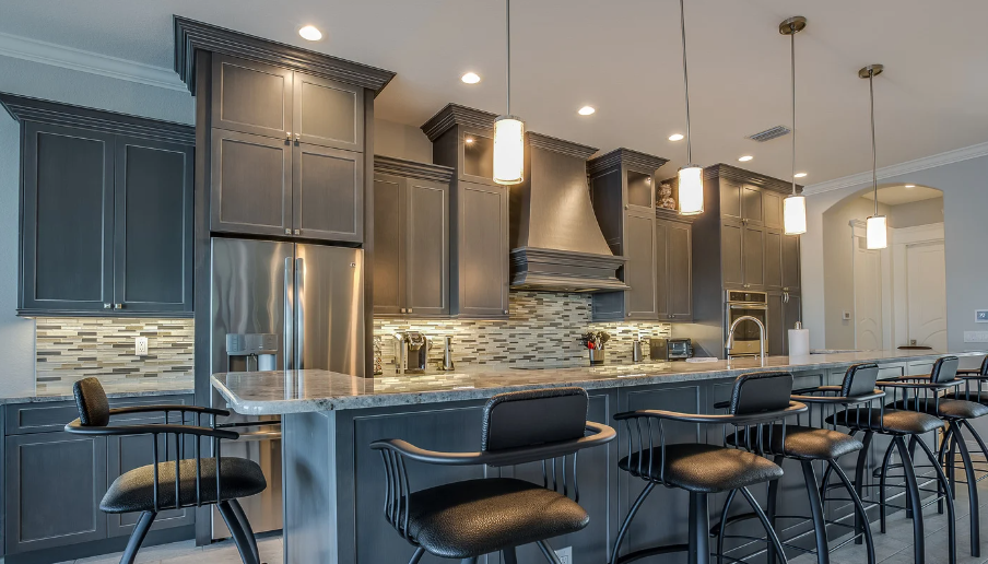 A kitchen with gray cabinets , stainless steel appliances , a large island and bar stools.