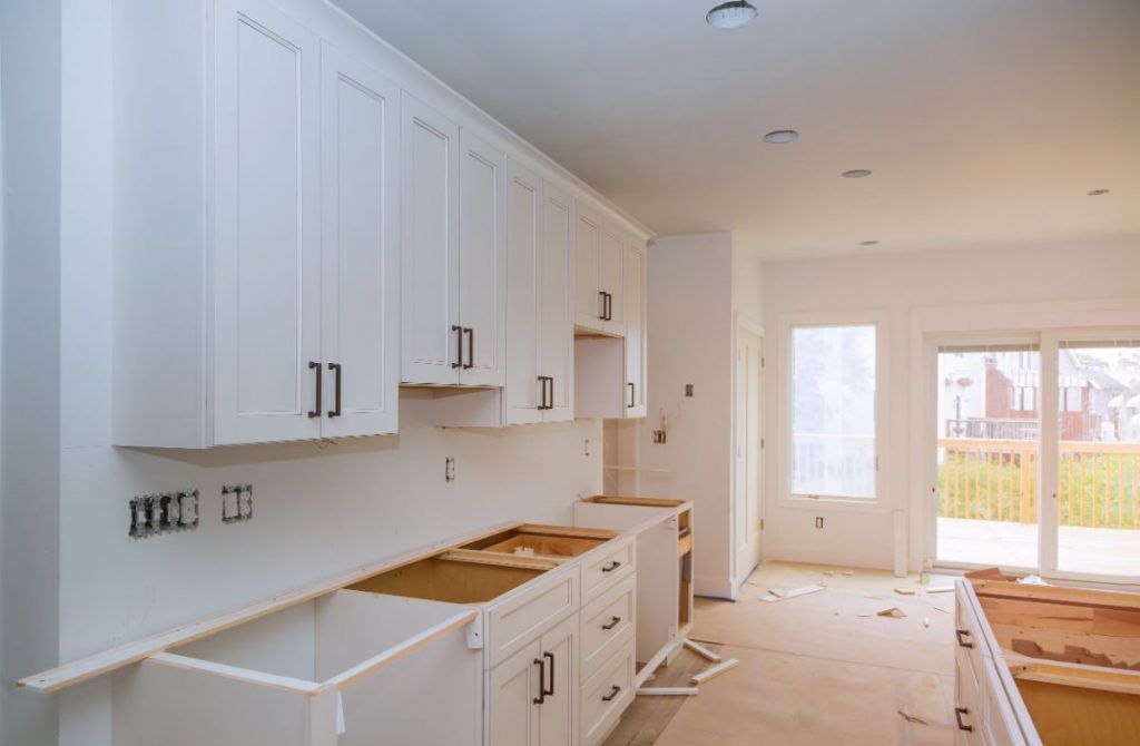 A kitchen under construction with white cabinets and sliding glass doors.