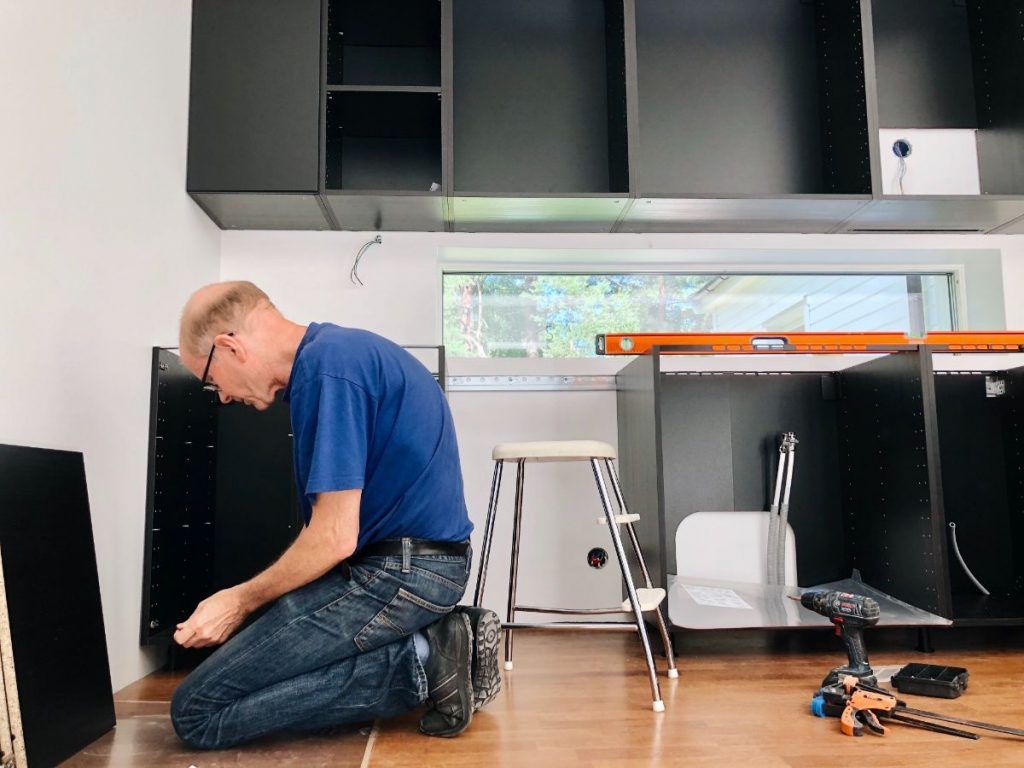 A man is kneeling down in a kitchen working on a cabinet.