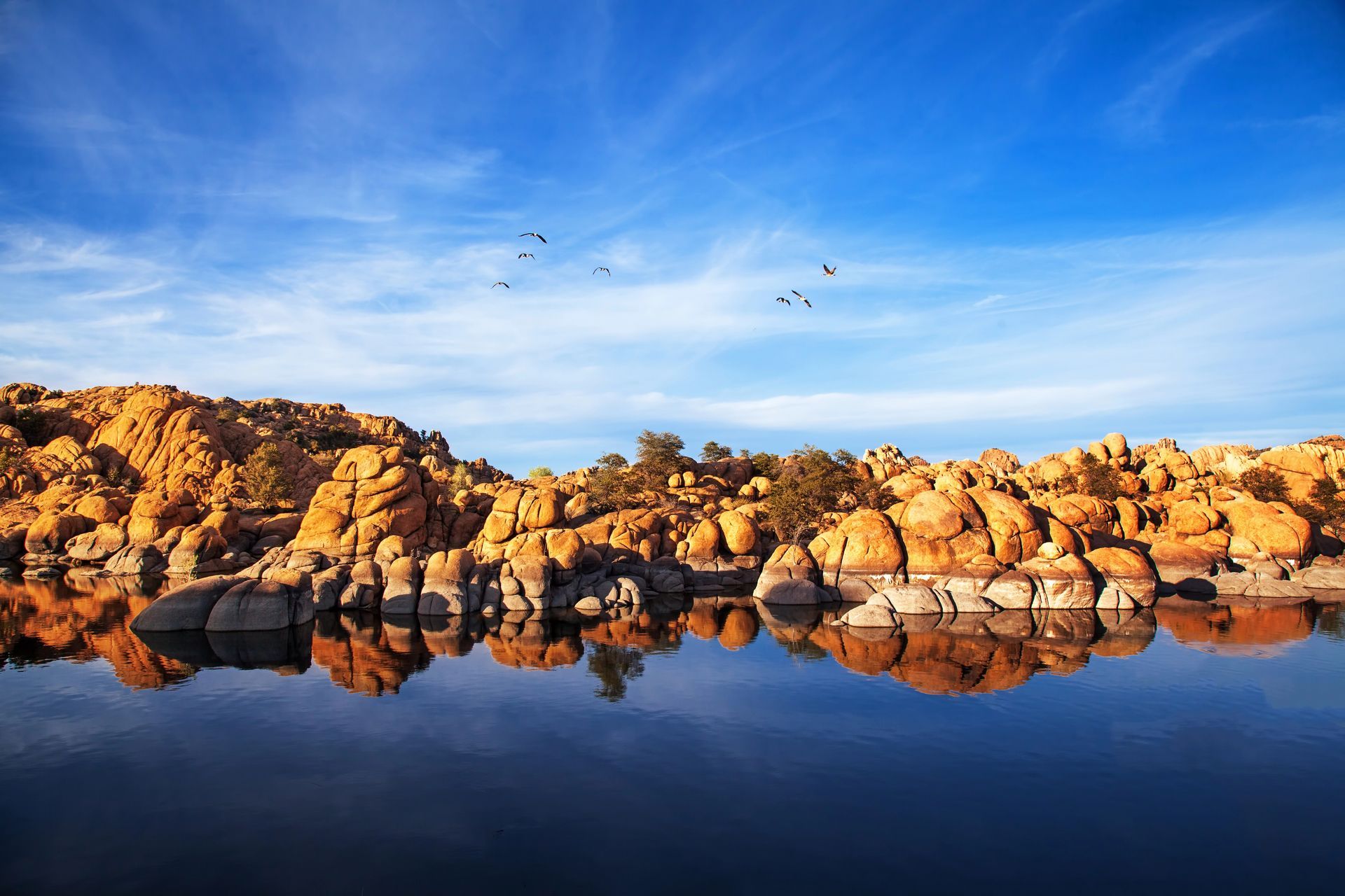 A lake with rocks in the background and birds flying over it.