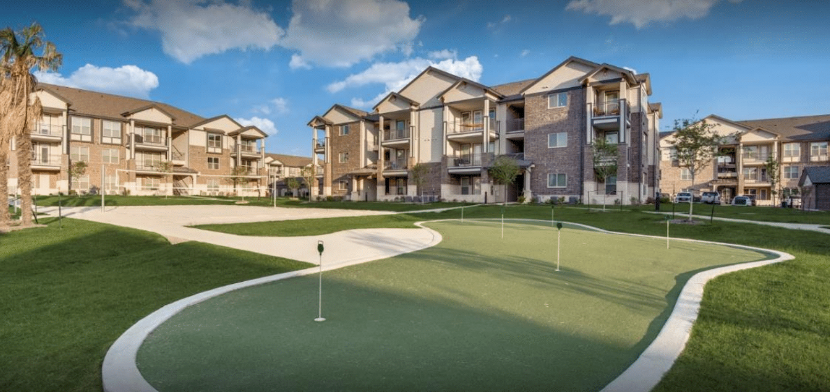 Apartment complex courtyard with a green putting area and beige buildings under a blue sky