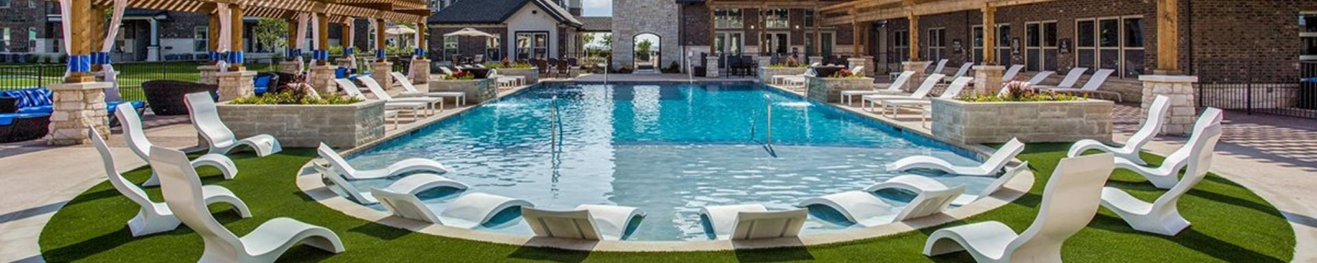 Resort pool with blue water, white lounge chairs, and umbrellas beside a multi-story hotel at sunset