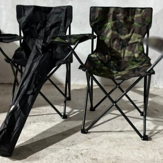 Dos sillas de camping plegables, una negra y otra camuflada, colocadas sobre hormigón.