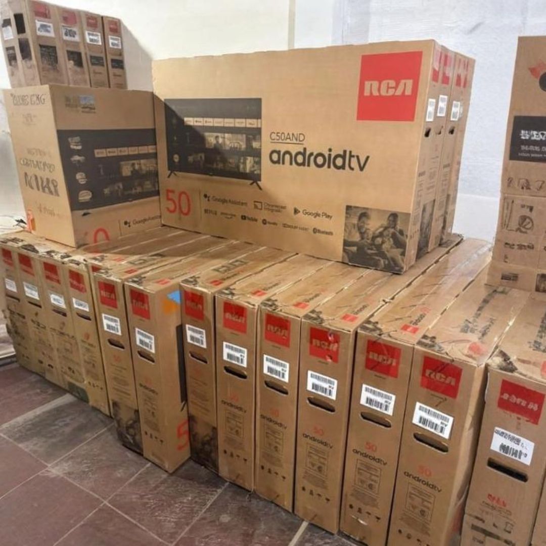 Cajas de televisores Android RCA apiladas en una habitación, listas para la venta.