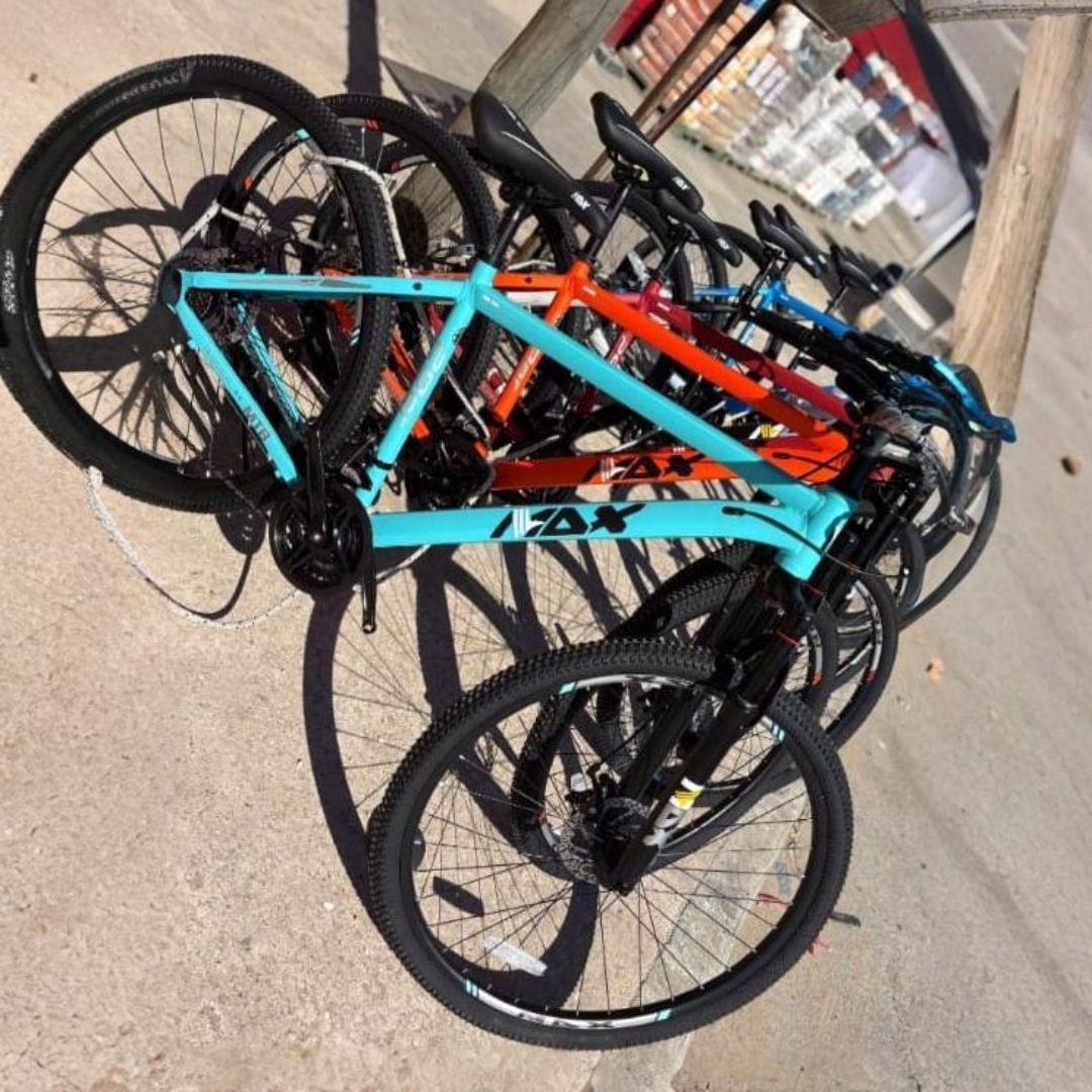 Bicicletas apoyadas en un poste; cuadros turquesa, naranja y azul; ruedas negras; estacionadas al aire libre.