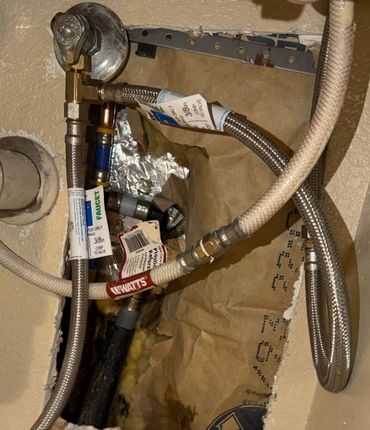 Plumbing connections with braided supply hoses and metal fittings installed inside an open wall cavity.