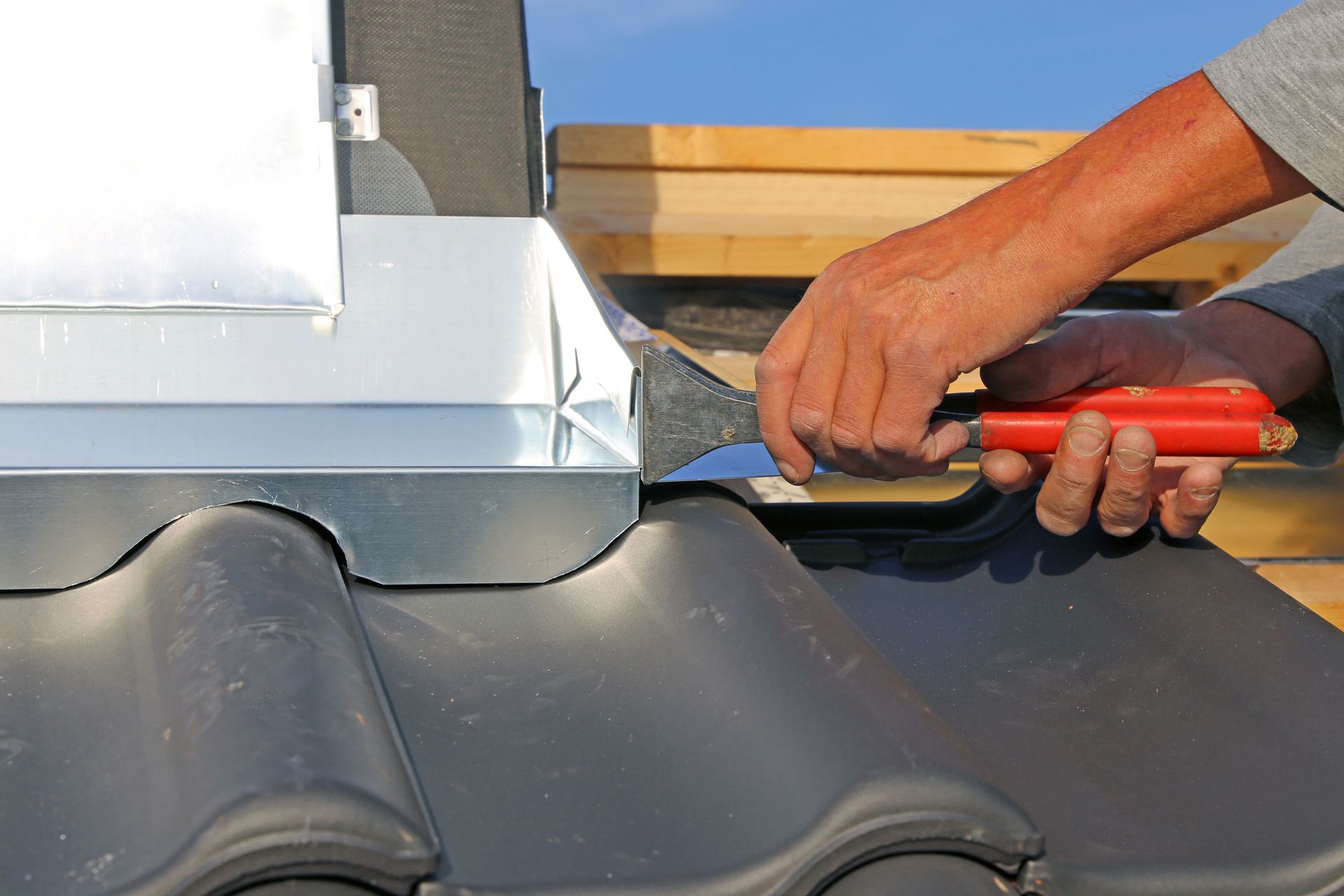 Person installing flashing on a tiled roof, using a tool.