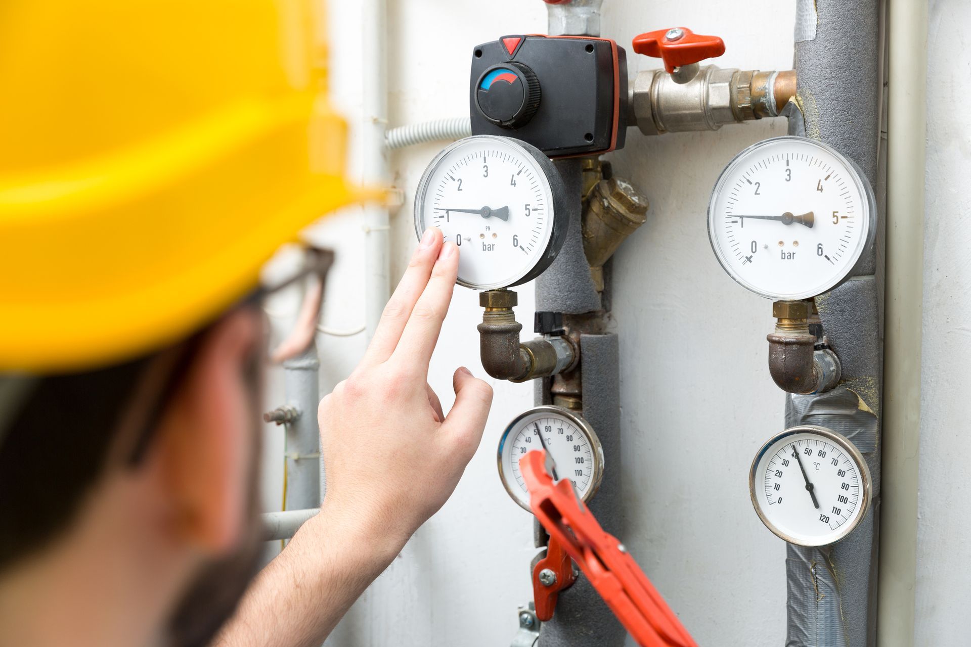Person in yellow hard hat checking gauges on pipes.