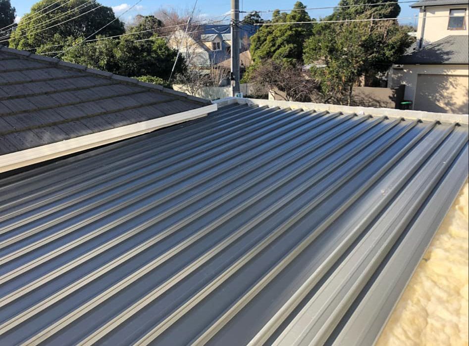 New corrugated metal roof with grey panels next to a tile roof.