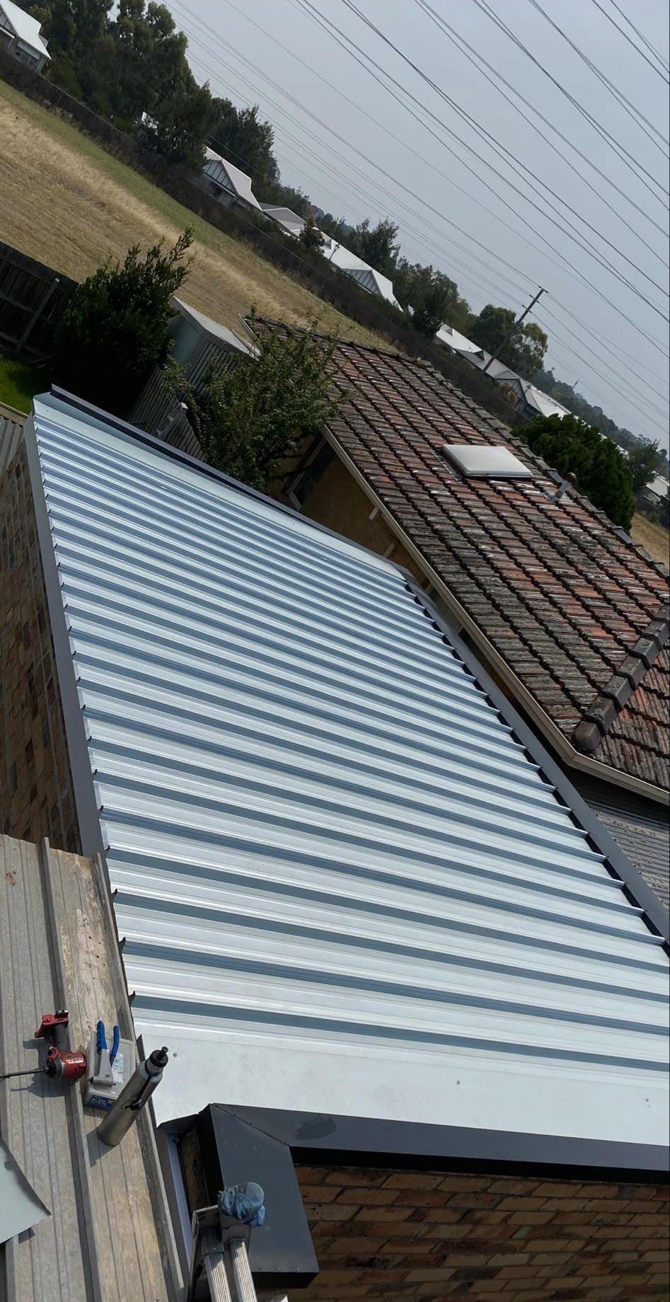 Newly installed metal roof on a building, with a view of another tile roof and a field in the distance.