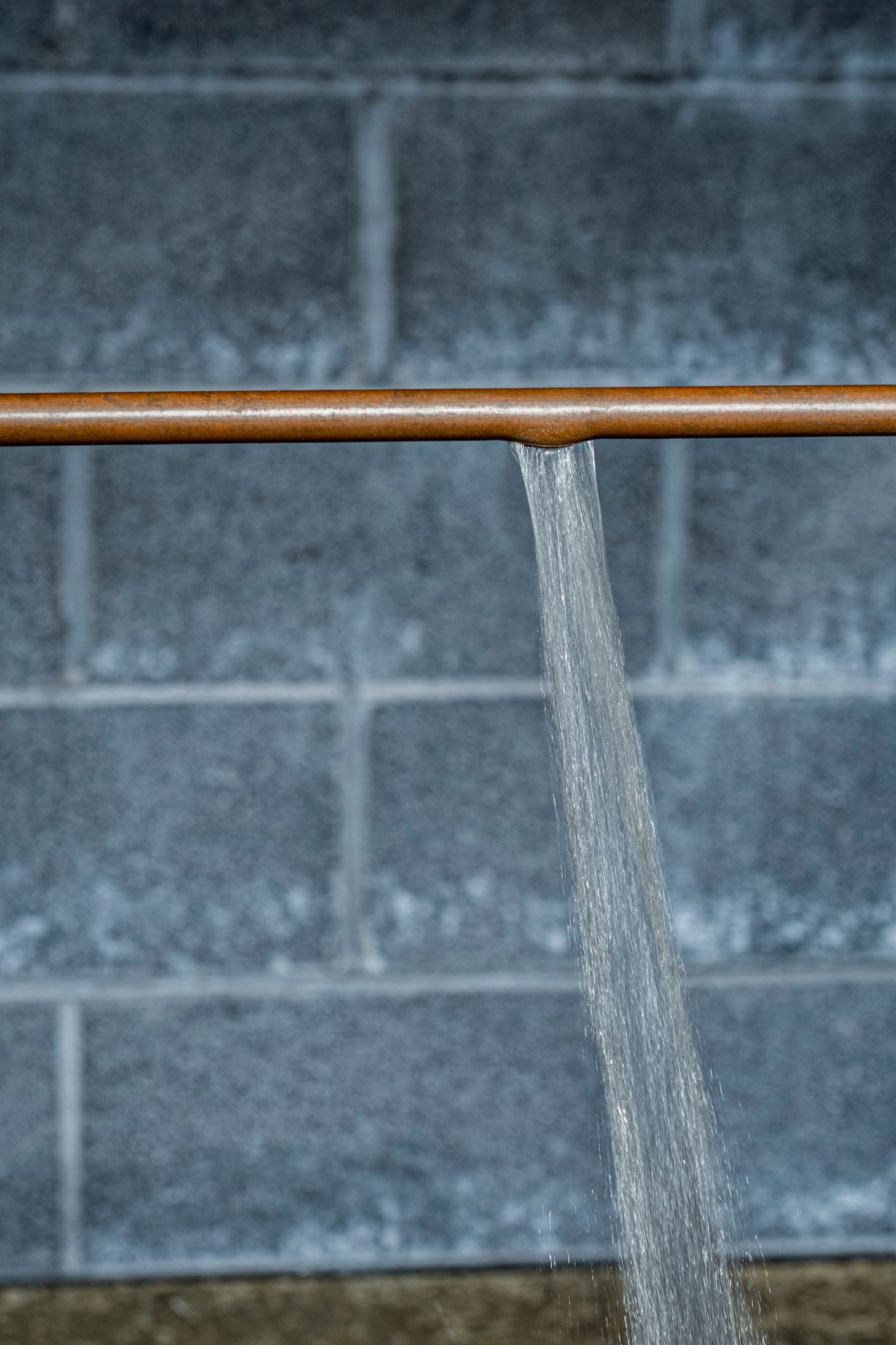 Plumber using a wrench to fix a leaky white pipe under a sink. Water is spraying.