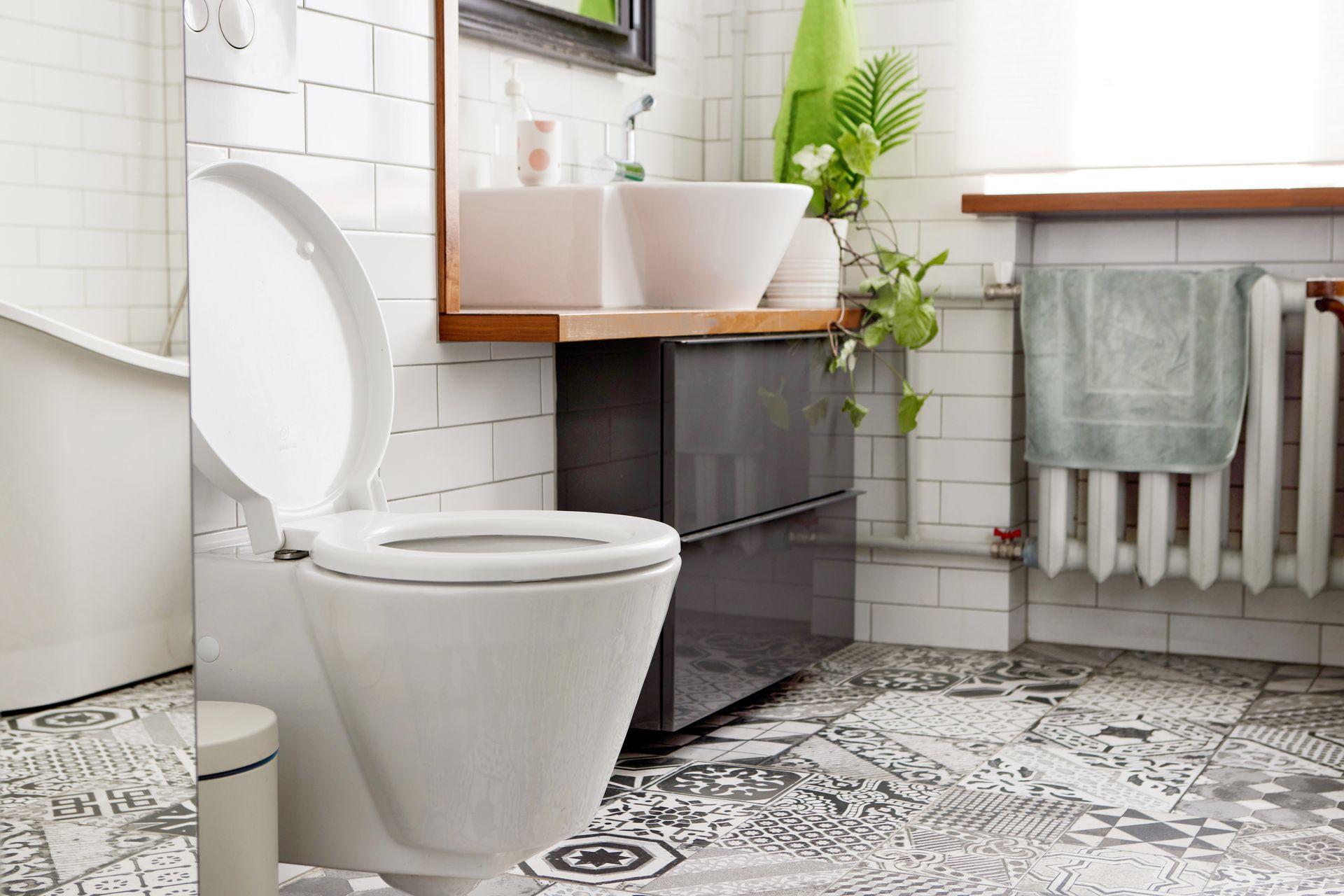 White toilet with open lid in a modern bathroom with patterned floor tiles and a sink.