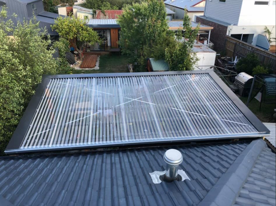 Solar hot water panels on a dark gray rooftop, surrounded by trees and houses.