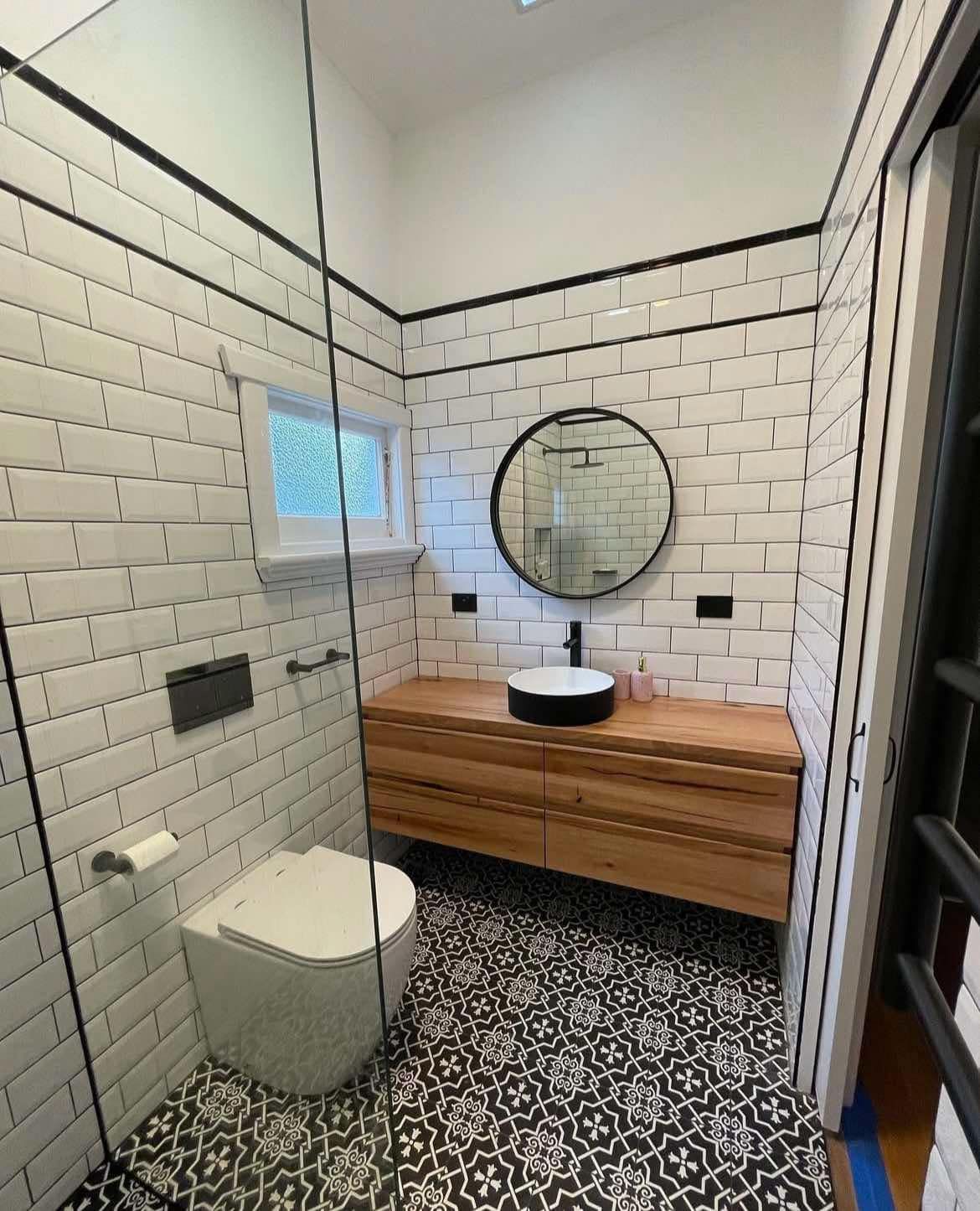 Modern bathroom with white brick tiles, black trim, wood vanity, and patterned floor.