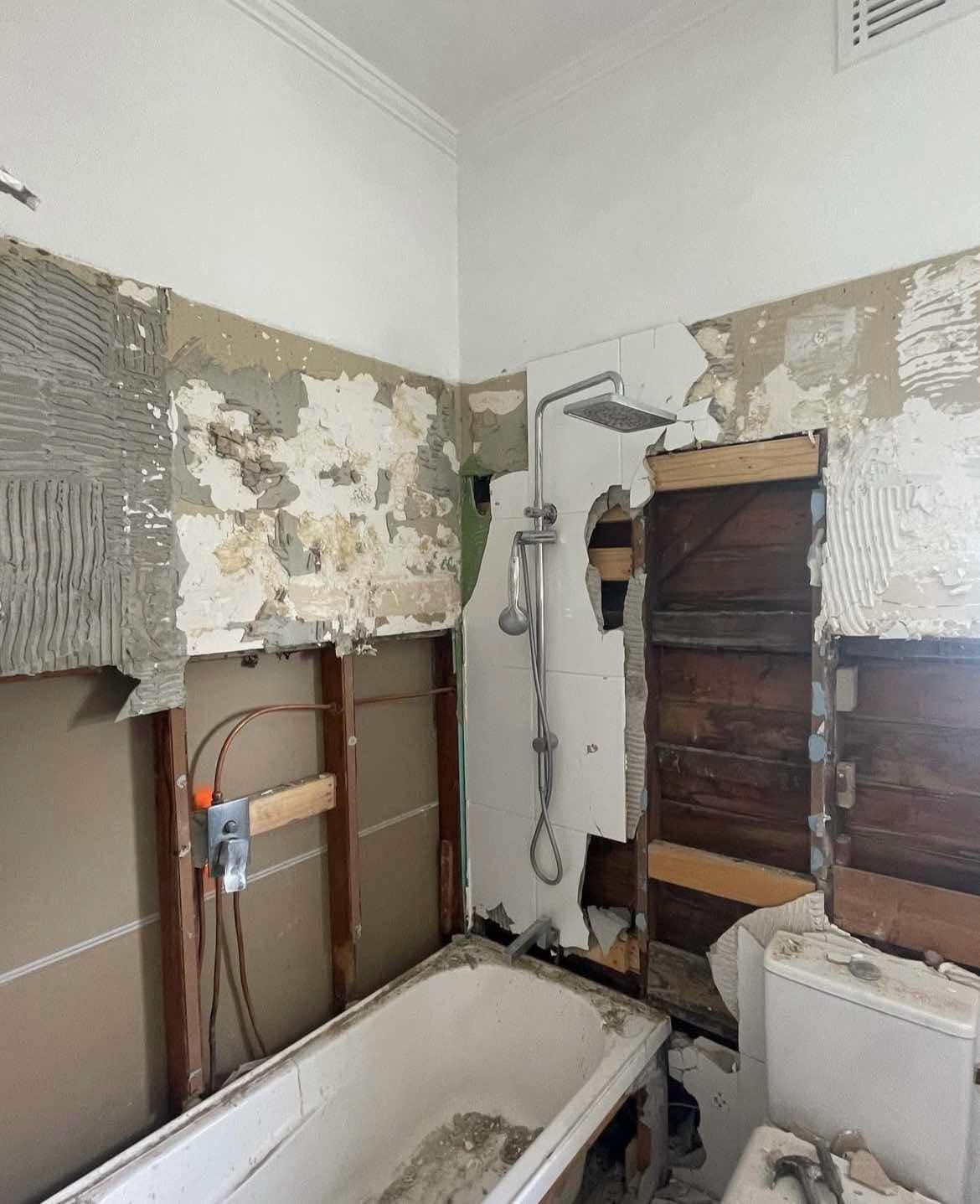 Bathroom undergoing renovation; damaged walls, exposed plumbing, and a shower fixture remain.