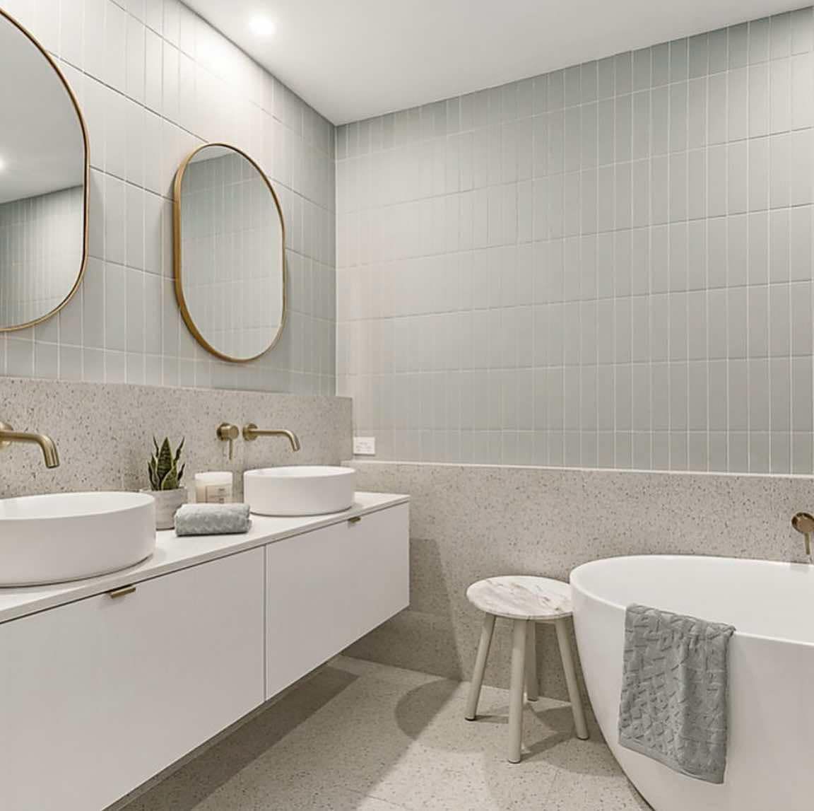 Modern bathroom with white vanity, round sinks, gold fixtures, and oval mirrors.