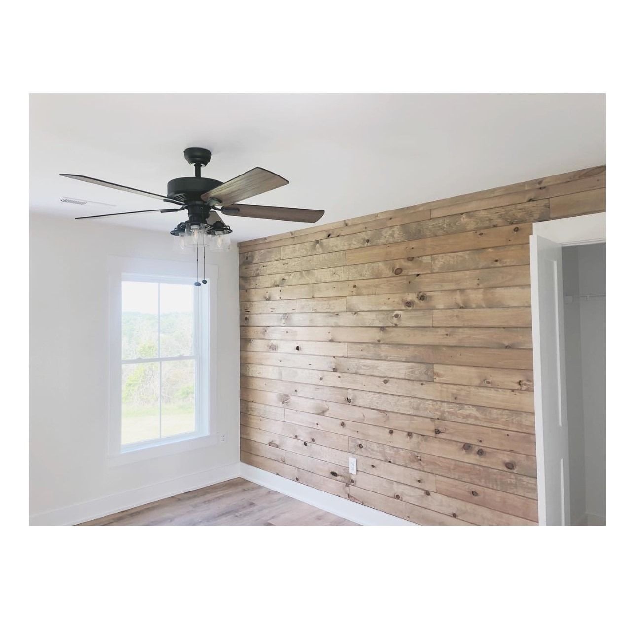 Bedroom with wood plank accent wall, white walls, and a ceiling fan.