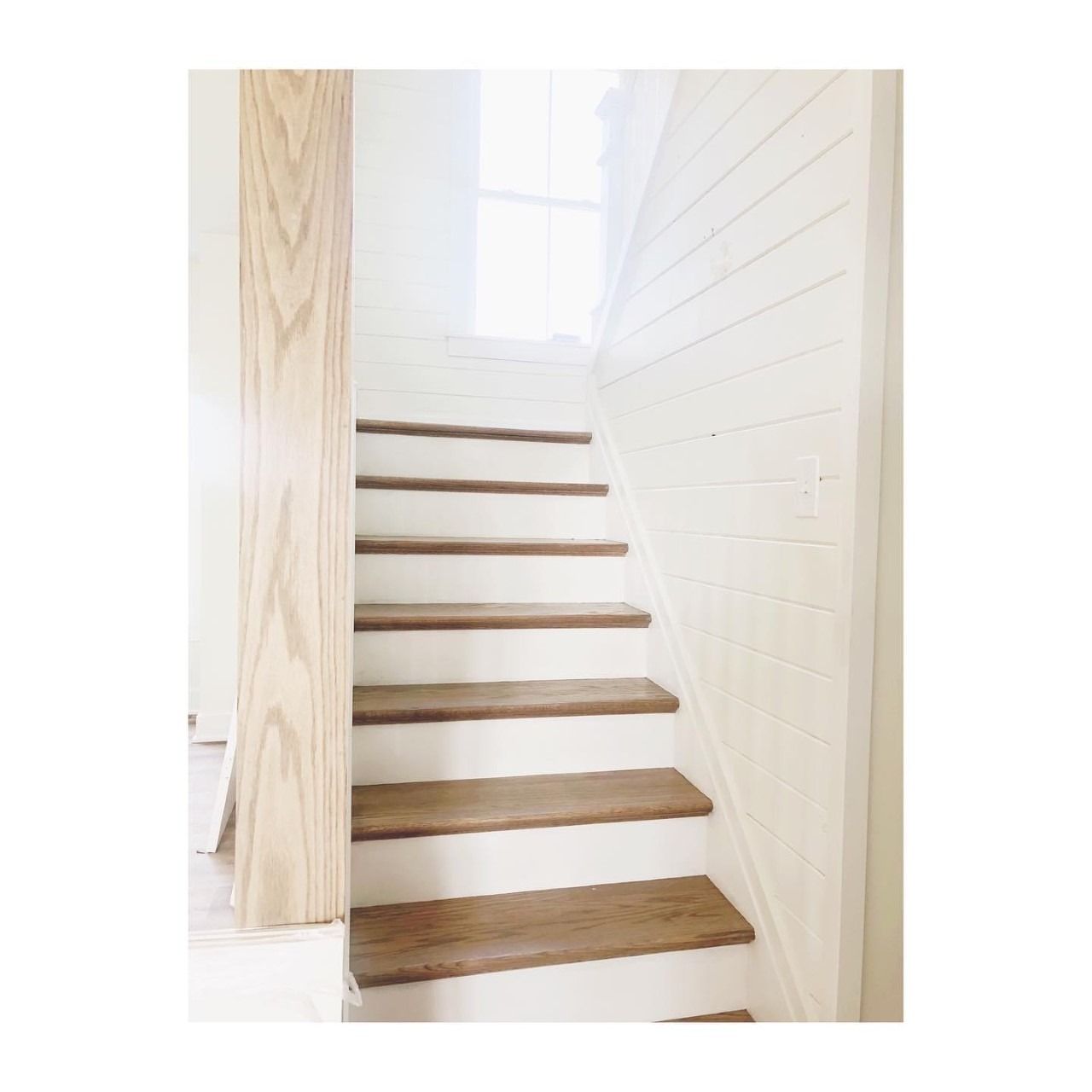 Wooden stairs with white risers and a light-colored wood post next to them, set indoors.