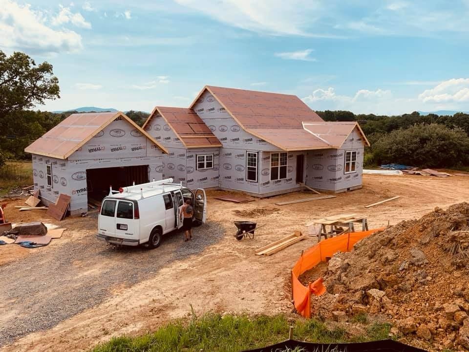 House under construction with a white van parked in front on a dirt lot, blue sky.