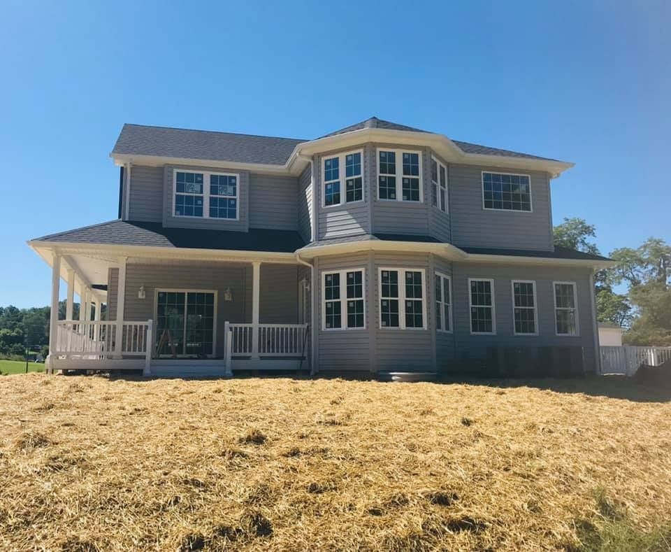Two-story gray house with white trim and wraparound porch against a clear blue sky.