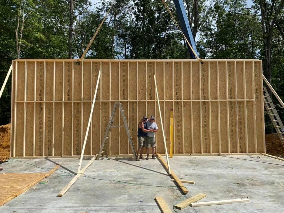 Large wooden wall frame under construction, two people standing in front of it.