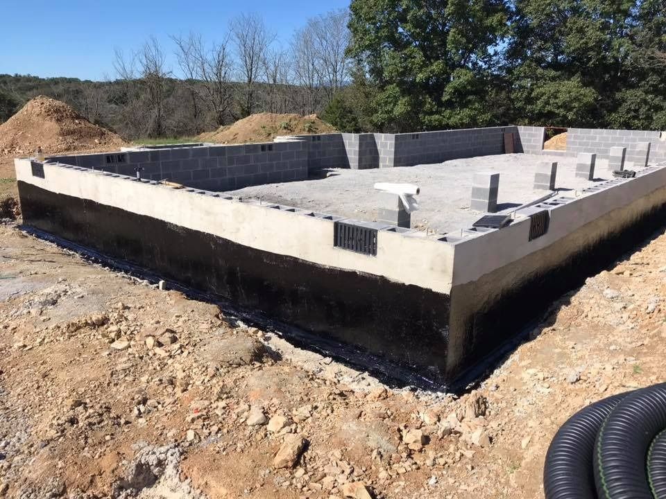 Foundation of a building under construction, made of concrete blocks and coated with black waterproofing.