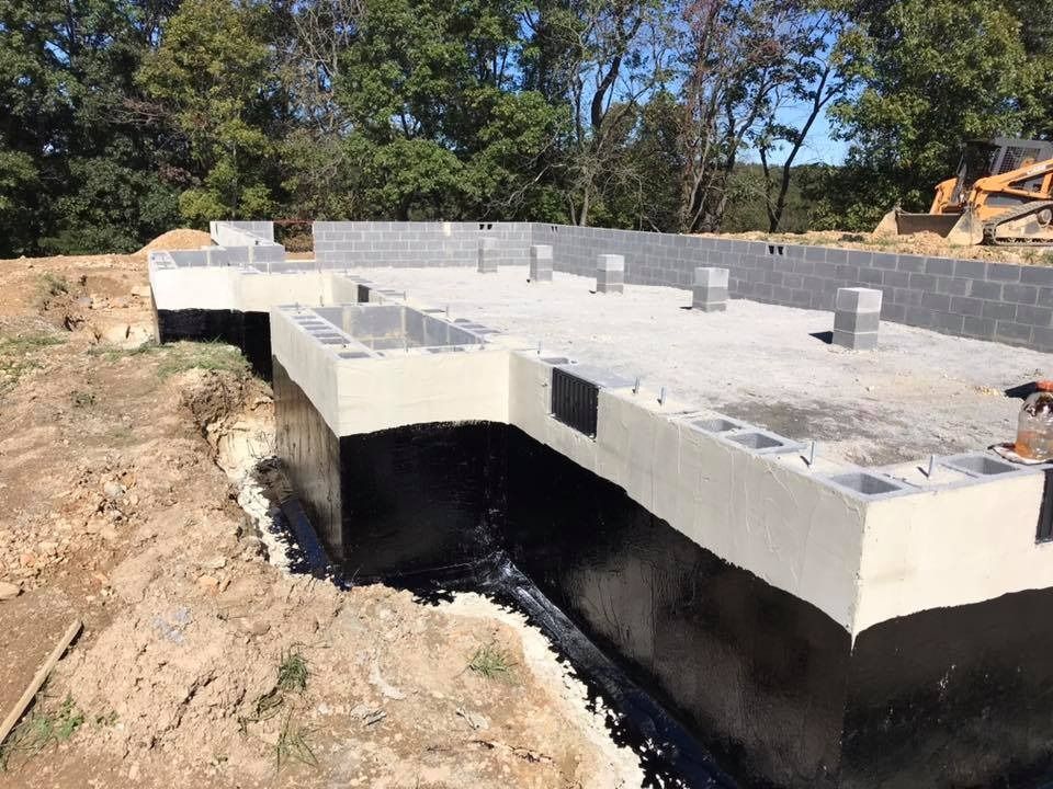 Foundation of a building under construction, cinder block walls, and black waterproofing, outdoors.