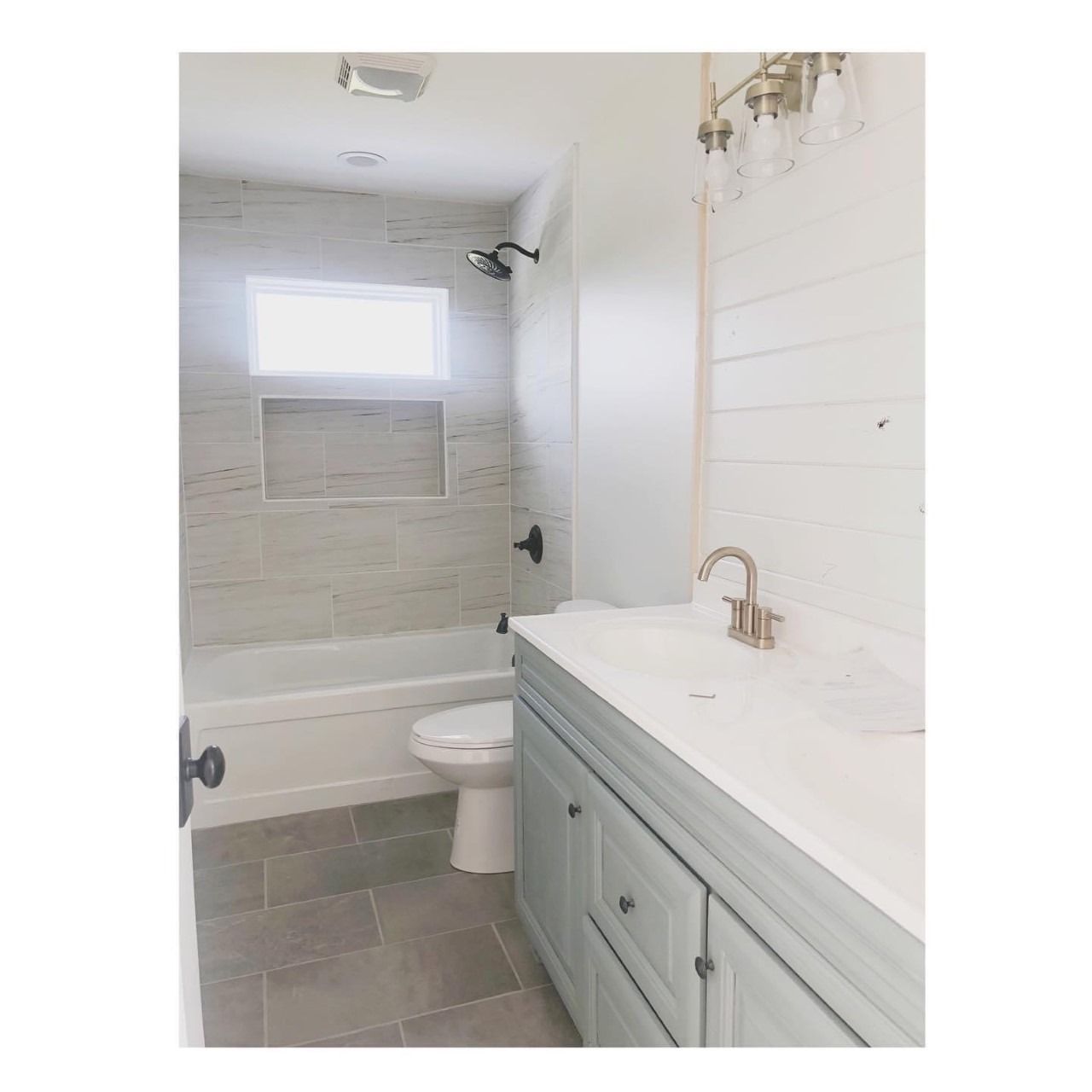 Bathroom with gray tile, white tub, light blue vanity, and silver fixtures.