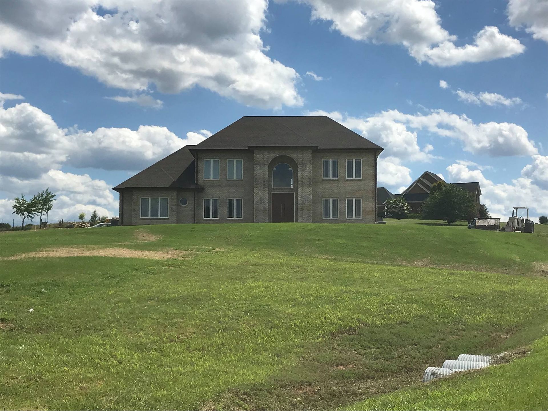 Two-story stone house on a grassy hill under a partly cloudy blue sky.
