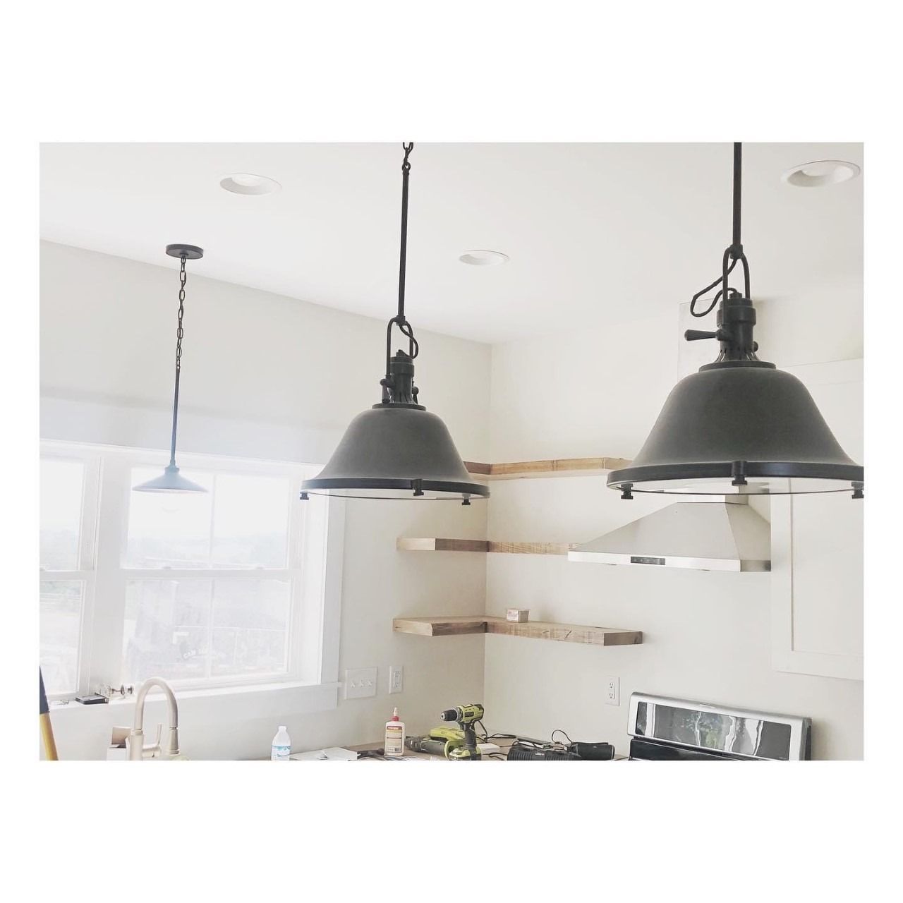 Kitchen with three hanging pendant lights, white walls, and wooden shelves.