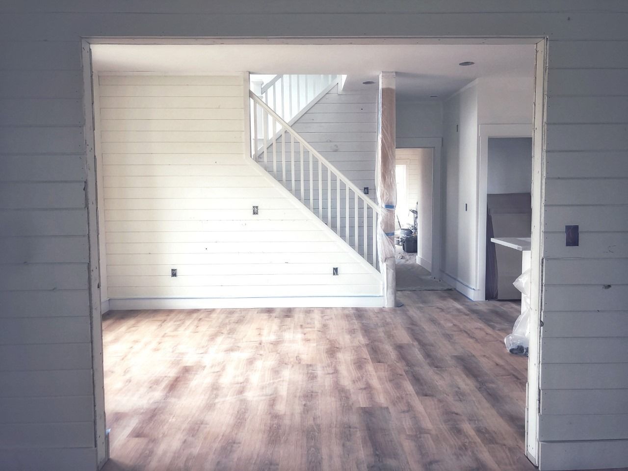 Interior view of a house with light wood flooring, a staircase, and shiplap wall.