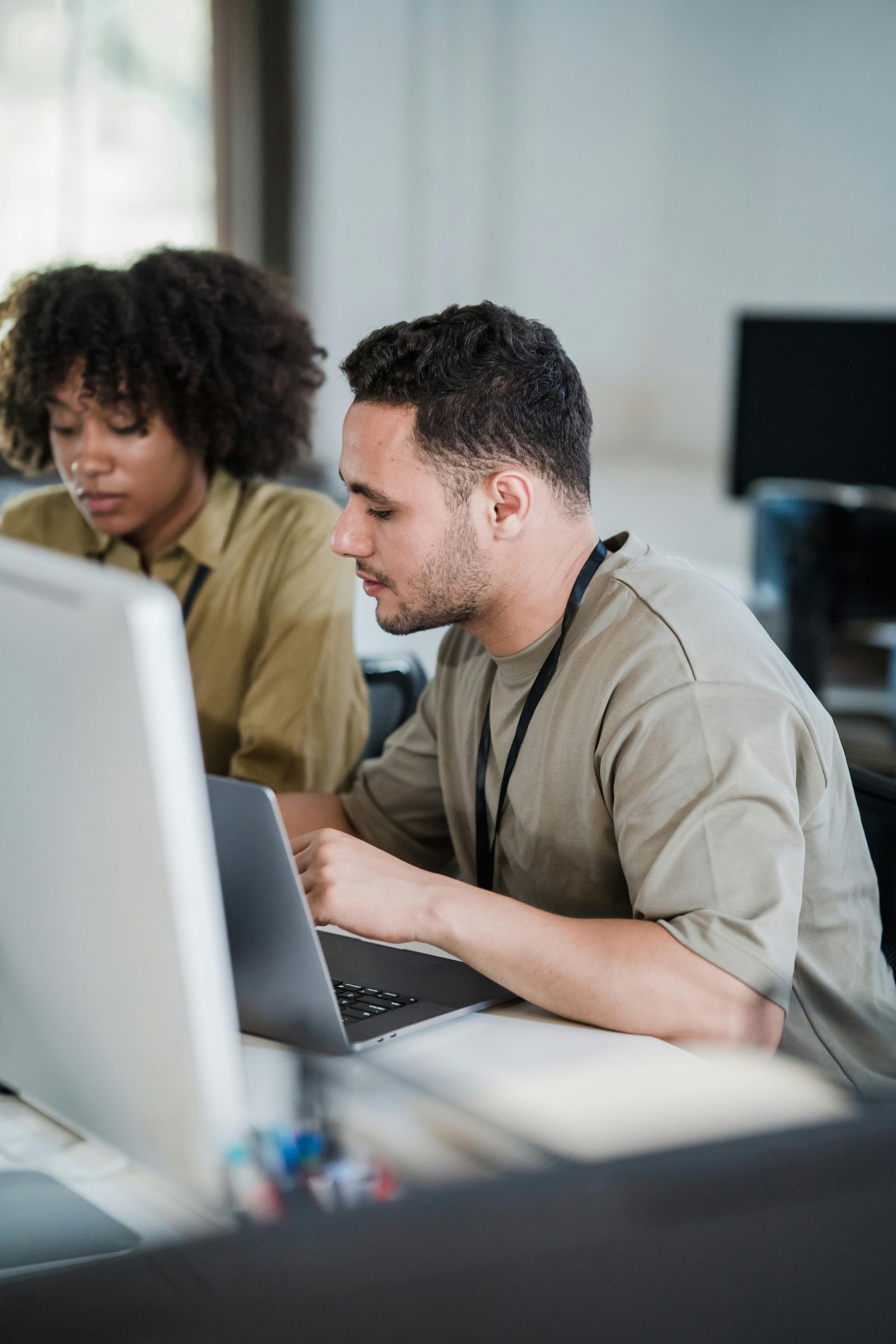 A man and a woman are sitting at a desk looking at a laptop computer.